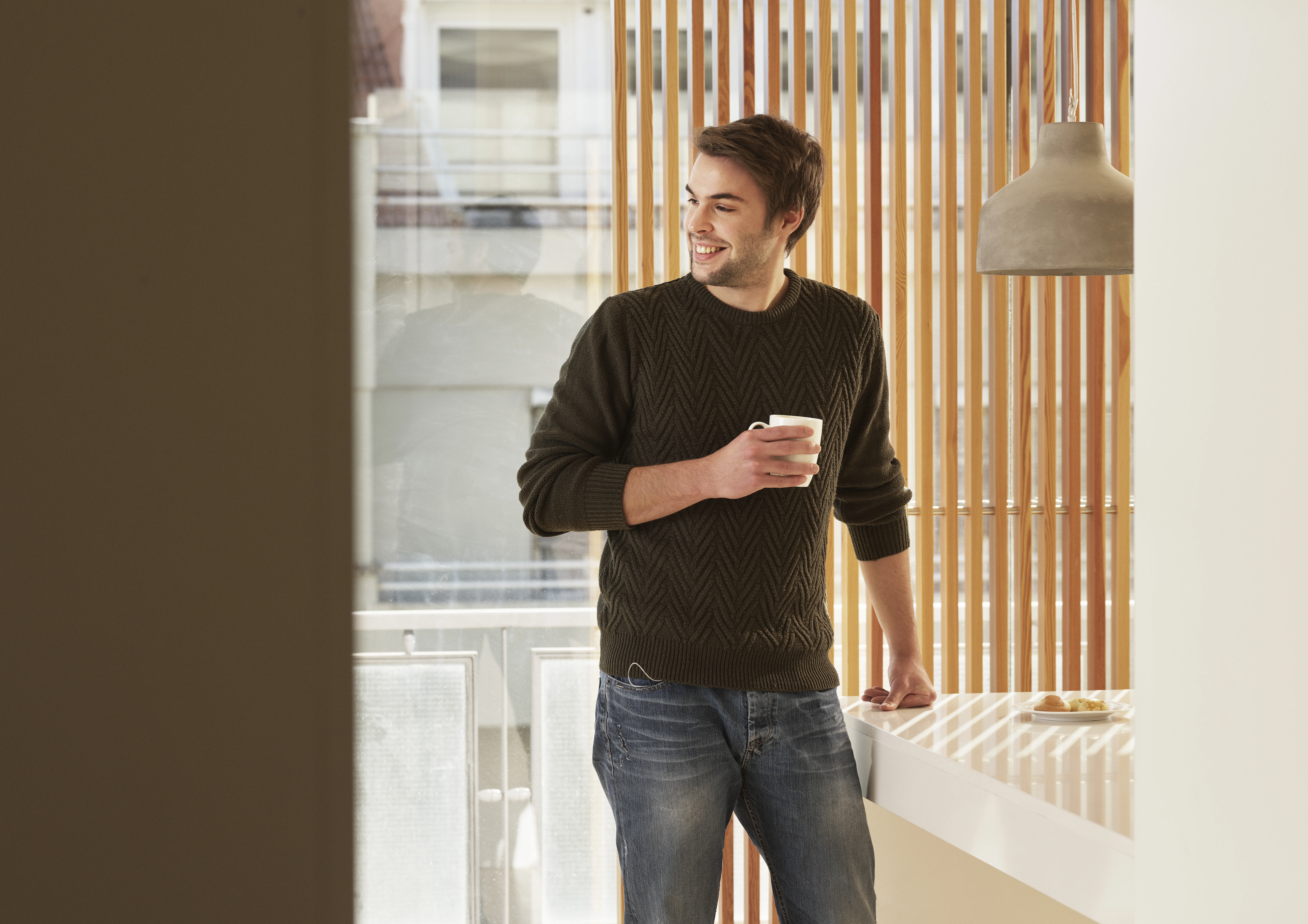 Eine Person, die vor einem Fenster steht und eine Tasse in der Hand hält